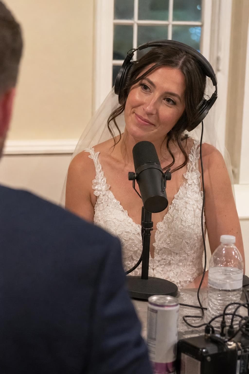 A bride in headphones smiling at the microphone during her wedding podcast interview