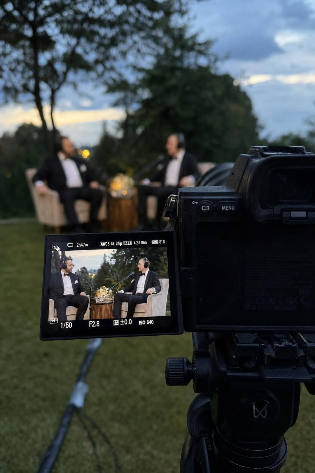 Our camera on a tripod framing two groomsmen in armchairs on its screen, outdoors at golden hour