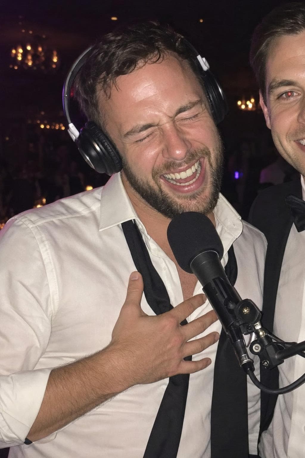 A groomsman in headphones laughing into the microphone during a late-night interview